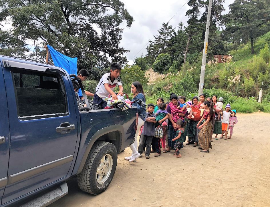 A volunteer in the back of a pickup truck handing out clothing to children from a Guatemalan village displaced by a volcanic eruption.